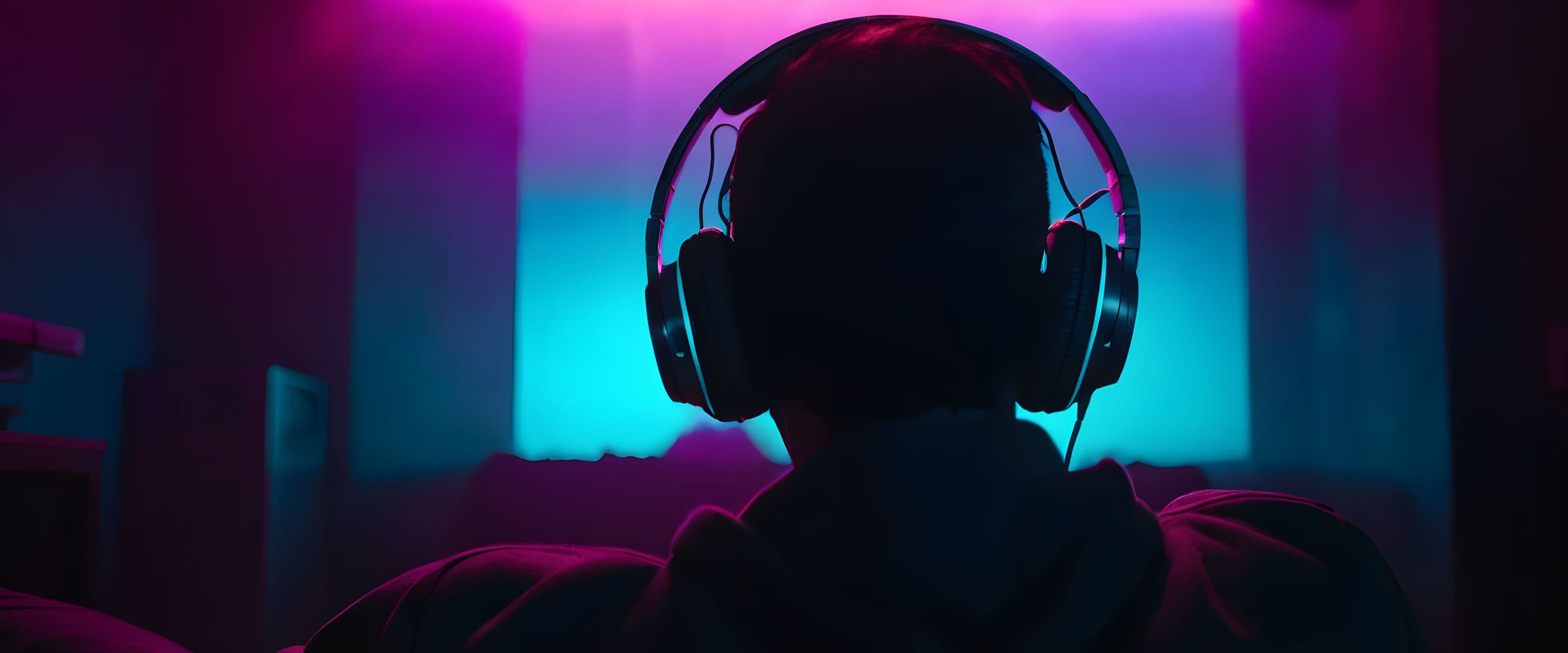 Person wearing headphones in a dark room bathed in cyan and magenta light